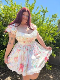 a woman in a pink and white dress posing in front of bushes